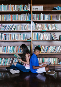 duas criaças sentadas na frente de uma estante de livro viradas uma de costas para outra